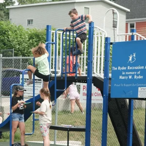 Children playing on a blue and white playground, climbing, sliding, and interacting on a sunny day.