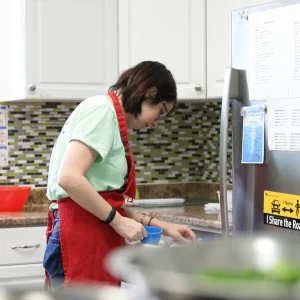 A person wearing an apron prepares food in a kitchen, measuring ingredients.