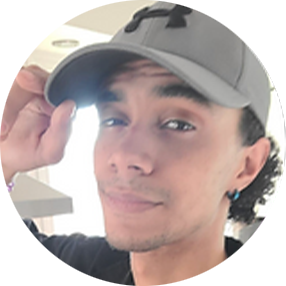 A man wearing a Under Armour cap, tilting it slightly while smiling at the camera.